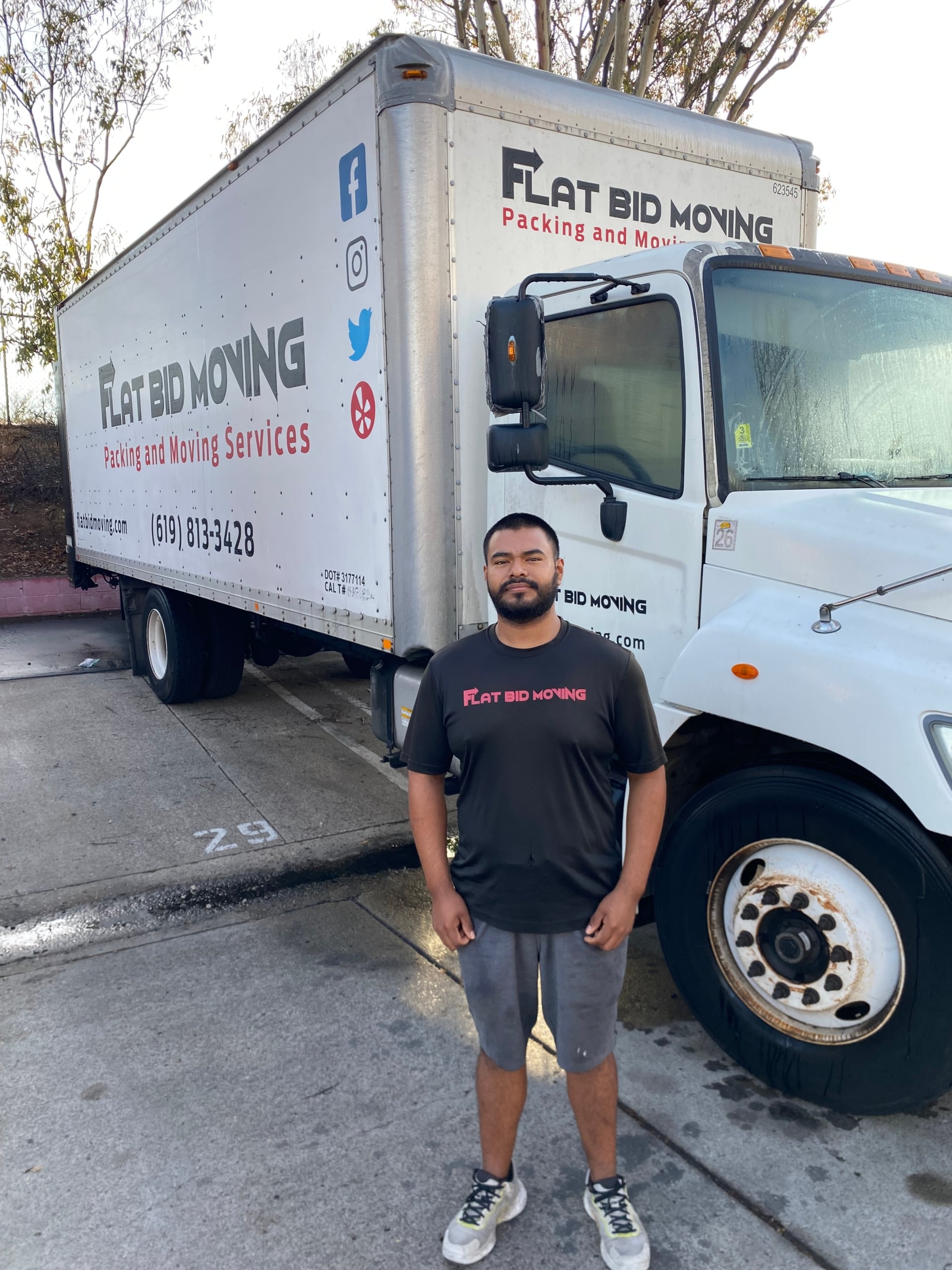 Flat Bid Moving LLC mover standing in front of a large moving truck parked in a lot with other company vehicles.