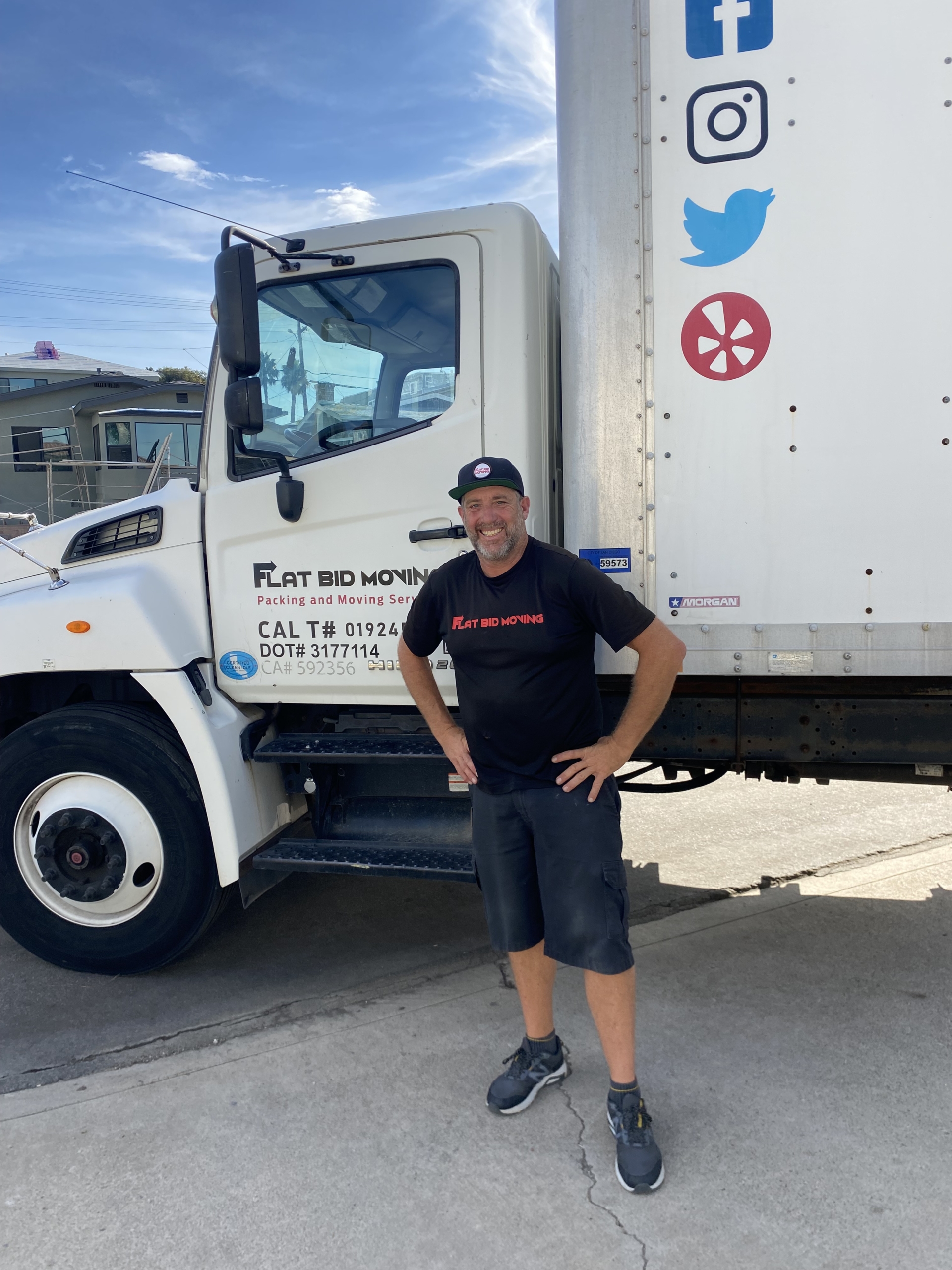 Flat Bid Moving LLC mover smiling while standing next to a branded moving truck in a residential area.