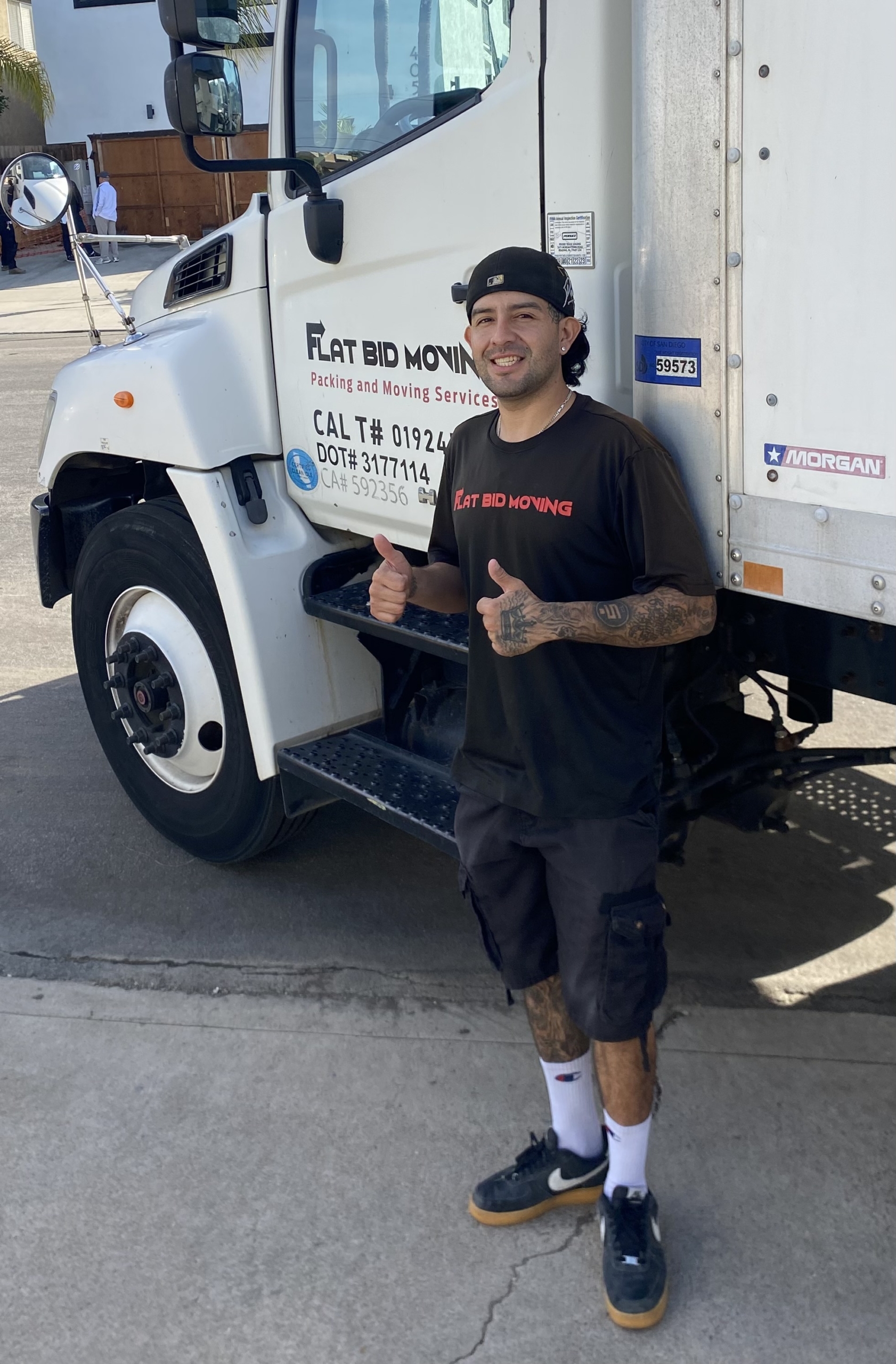 Flat Bid Moving LLC mover giving a thumbs-up while standing next to a large branded moving truck.
